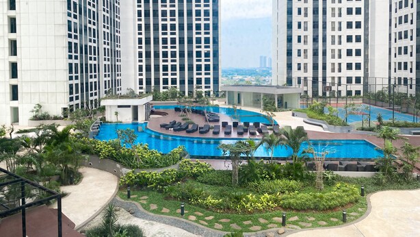 A high-rise residential building with a swimming pool, outdoor seating, and greenery. - Cozy Studio Room At Pollux Chadstone Apartment (Cikarang)