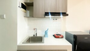 A modern kitchen with a stainless steel sink, wooden cabinets, a black range hood, and a black refrigerator. - Cozy Studio Room At Pollux Chadstone Apartment (Cikarang)