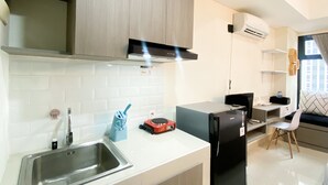A modern kitchen with a stainless steel sink, a black refrigerator, and wooden cabinets. - Cozy Studio Room At Pollux Chadstone Apartment (Cikarang)