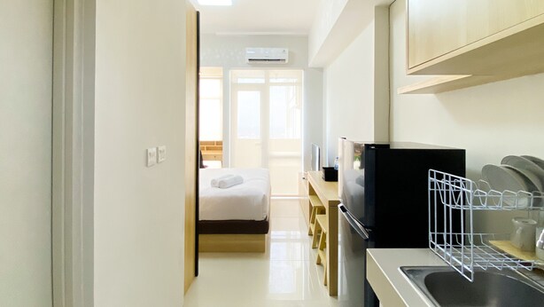 A modern kitchen with a refrigerator, sink, and dish rack. There is a bed with a white comforter in the background. - Best Deal And Comfy Studio Vasanta Innopark Apartment (Cikarang)