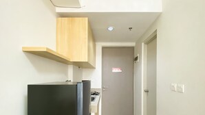 A narrow kitchen with a black refrigerator, a wooden cabinet, and a door with a red sign. - Best Deal And Comfy Studio Vasanta Innopark Apartment (Cikarang)