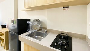 A compact kitchen with a stainless steel sink, a black stove, and a dish rack. - Best Deal And Comfy Studio Vasanta Innopark Apartment (Cikarang)
