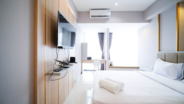 Una habitación de hotel moderna con una cama, un escritorio con silla, un televisor de pantalla plana montado en la pared y un equipo de aire acondicionado en el techo.