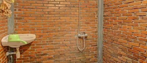 Un área de ducha pequeña y cerrada con pared de ladrillo, un lavamanos blanco y piso de piedrecitas.