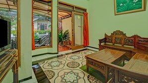 A room with a wooden sofa, a coffee table, and a patterned floor. There is a door leading to an outdoor area with plants. - Hotel O Villa Papada (Batu)