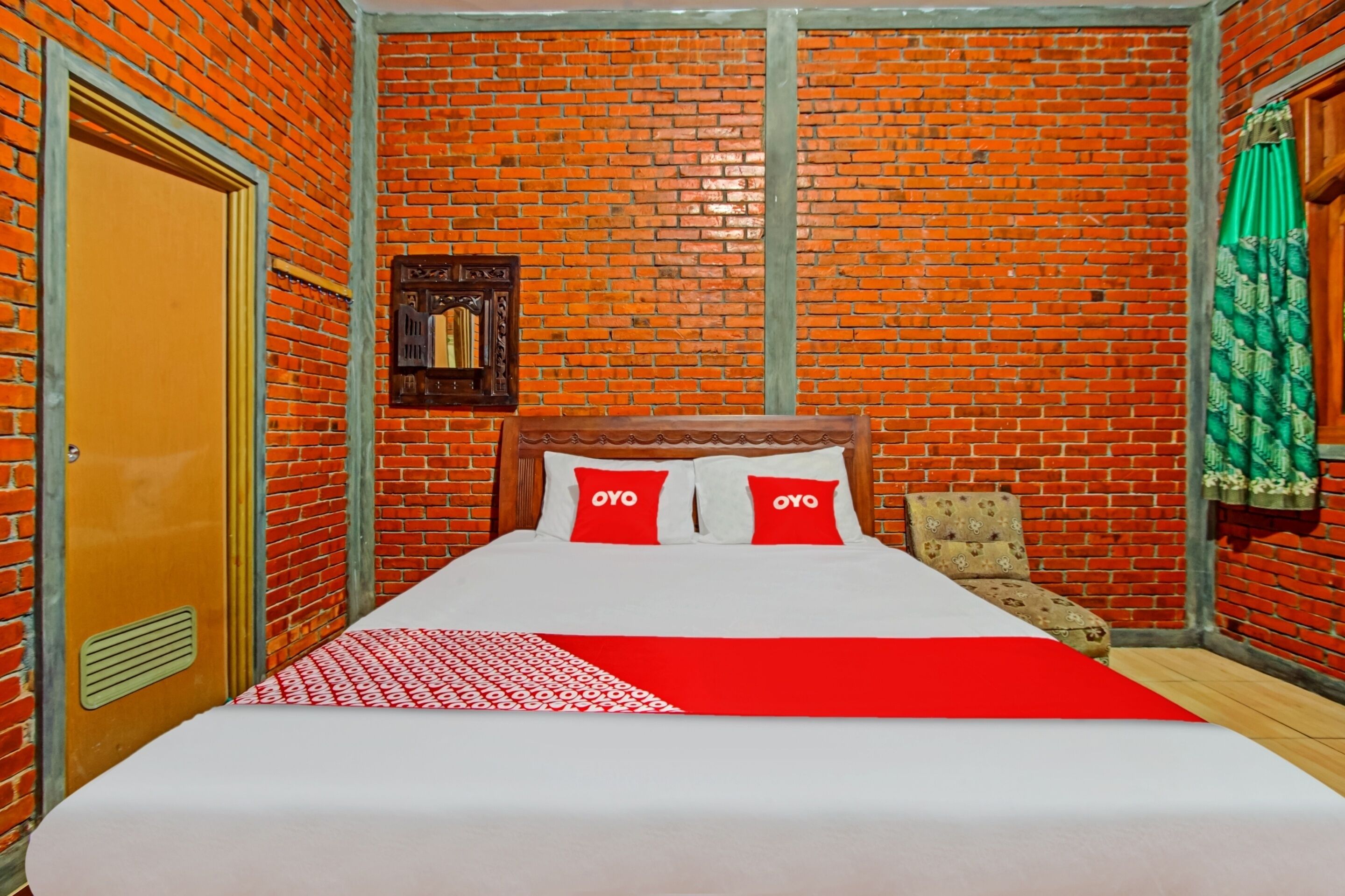 Una habitación con pared de ladrillo, cama de madera con ropa de cama roja y blanca, y una cortina verde.