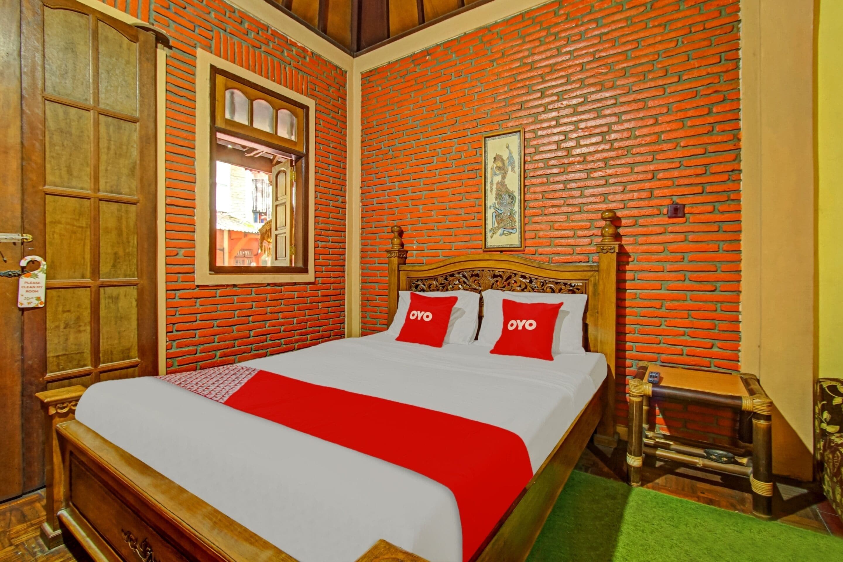 Ein Zimmer mit einer Ziegelwand, einem hölzernen Bett mit roter Bettwäsche, einem kleinen Holztisch und einem grünen Teppich.