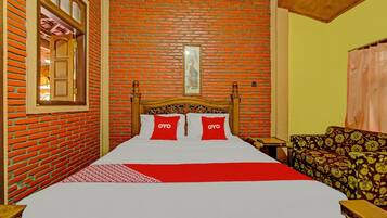 A room with a brick wall, a wooden bed with red pillows, a patterned sofa, and a framed picture on the wall.