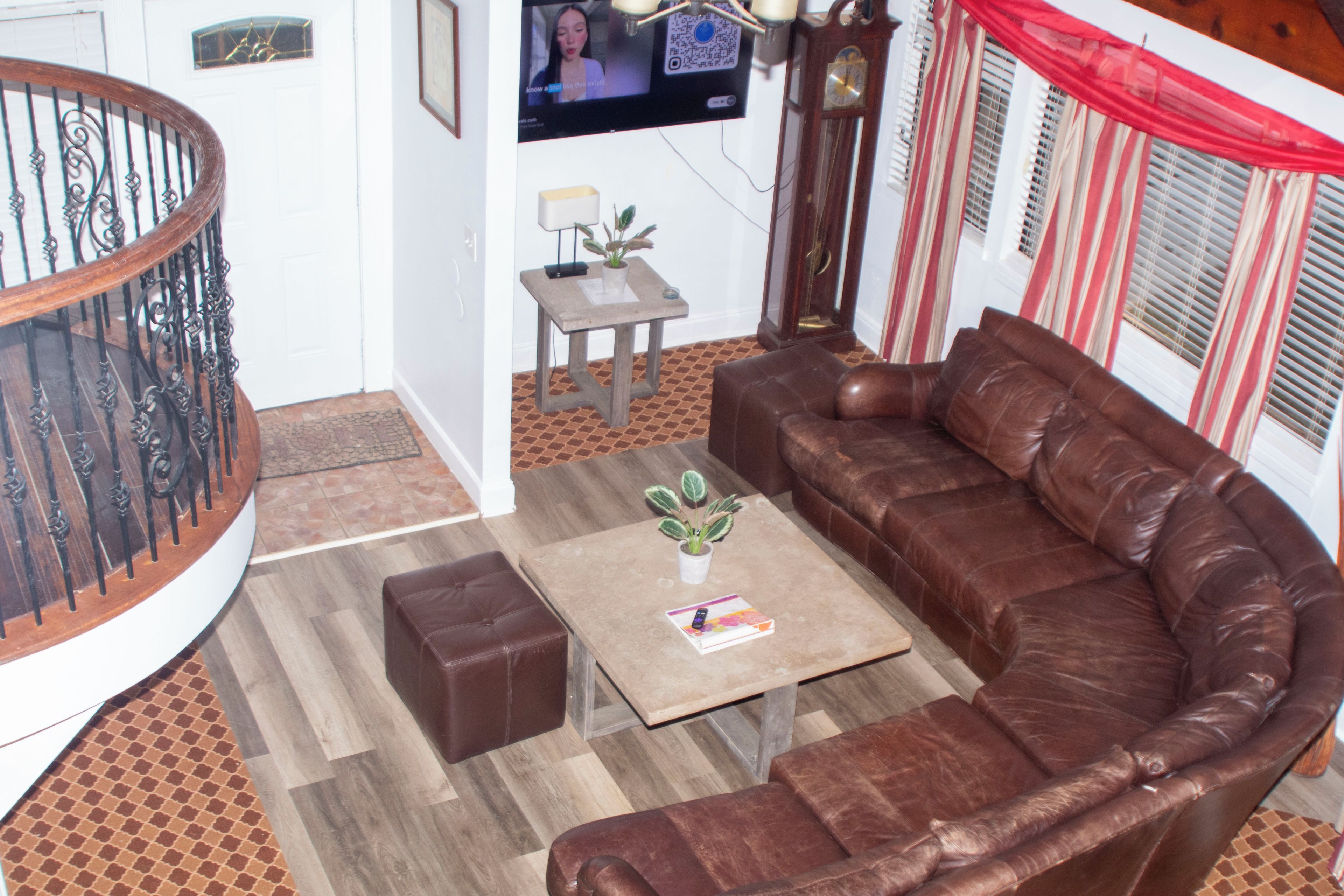 A living room with a brown leather sofa, a coffee table with a plant, a small table with a lamp, and a large wall-mounted TV.