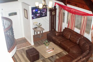 A living room with a brown leather sofa, a coffee table with a book and a plant, a TV mounted on the wall, and a staircase.