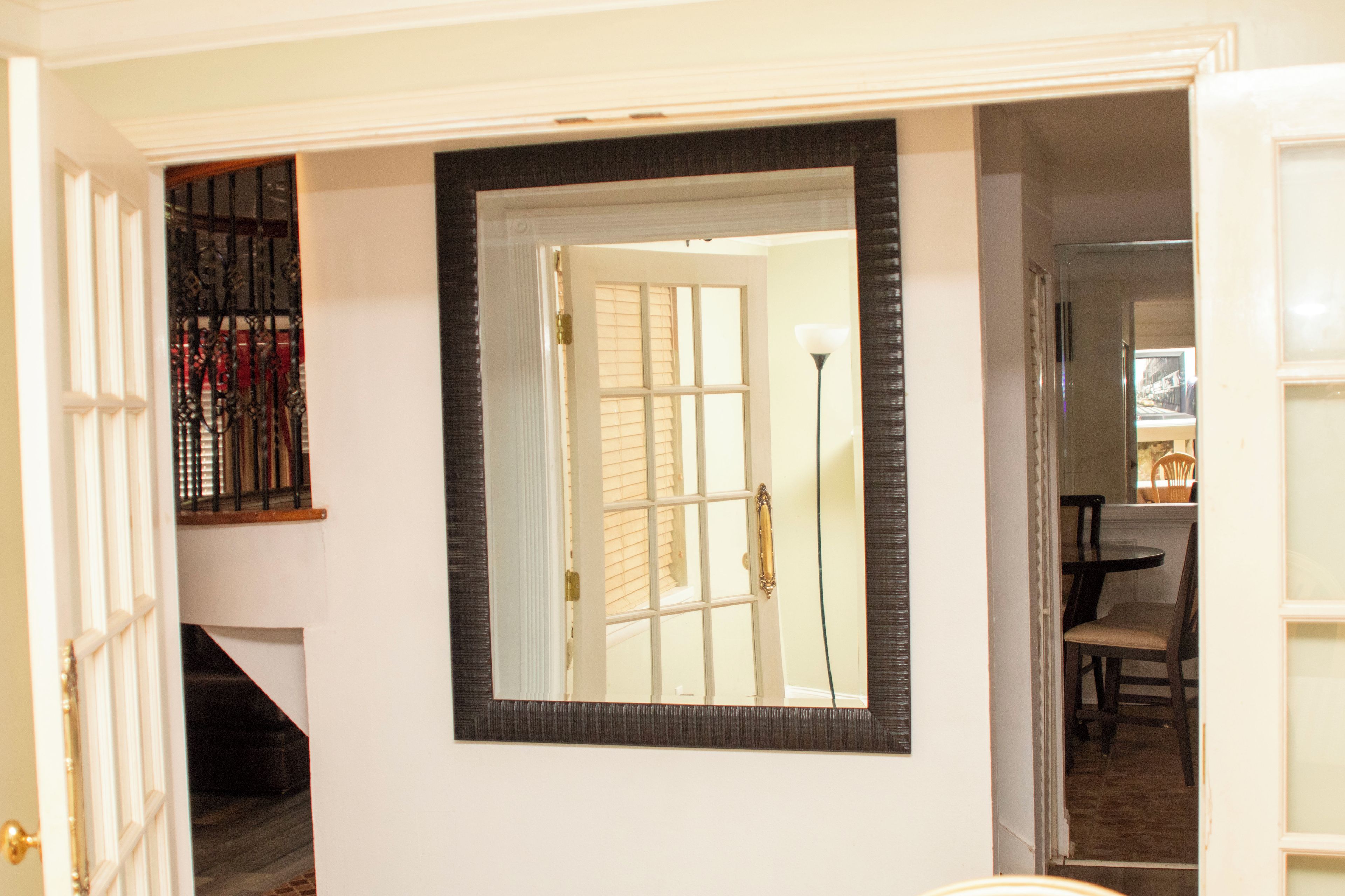 A hallway with a large mirror, a staircase, and a dining area visible through an open door.