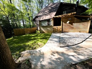 A wooden cabin with a garage, a concrete driveway, and a fenced yard. - Cheerful cabin, tucked away, for nature lovers. (Decatur)