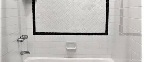 A bathroom with a white bathtub, a toilet, and a shower area with a black and white tiled design.