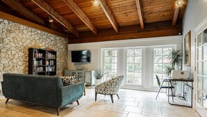 A spacious living room with a stone wall, a fireplace, a television, and a large window.