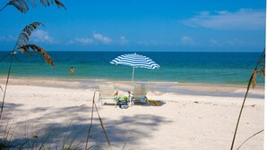 A beach with two beach chairs and an umbrella, a clear blue sky, and the ocean in the background.