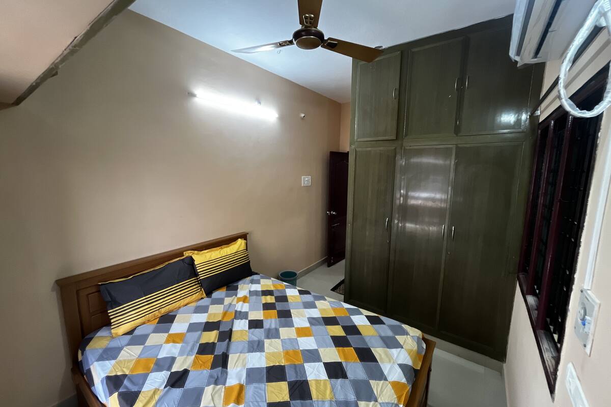 A bedroom with a bed, a wardrobe, a ceiling fan, and an air conditioning unit.