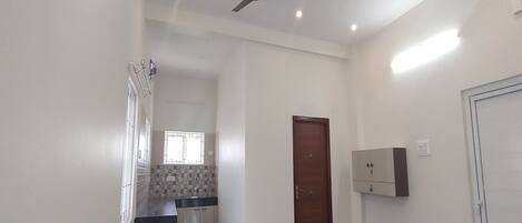 A spacious room with a ceiling fan, a kitchen area with a window, and a door leading to another room.