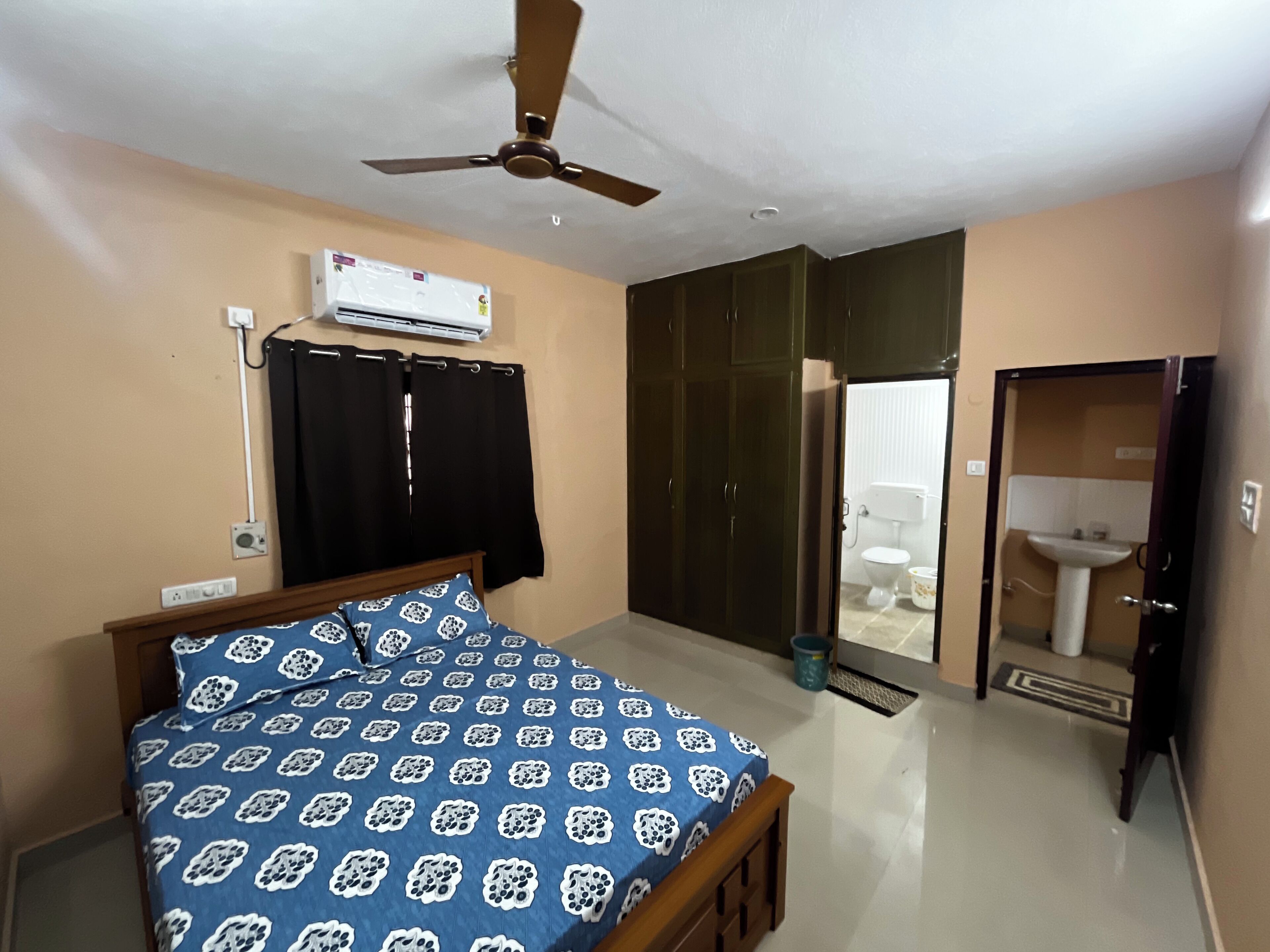 Una camera da letto con un letto, un condizionatore d'aria, una ventola a soffitto, un armadio e un bagno con lavandino e WC.