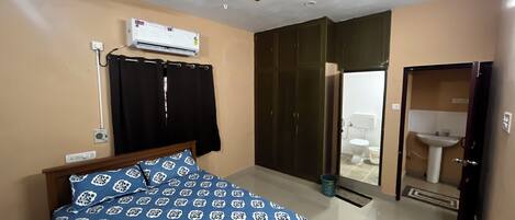 Una camera da letto con un letto, un condizionatore d'aria, una ventola a soffitto, un armadio e un bagno con lavandino e WC.