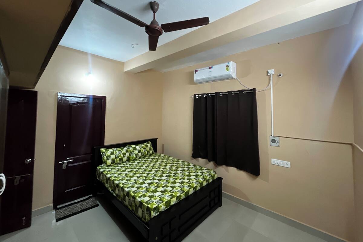 A bedroom with a bed, a ceiling fan, an air conditioning unit, and a dark door.