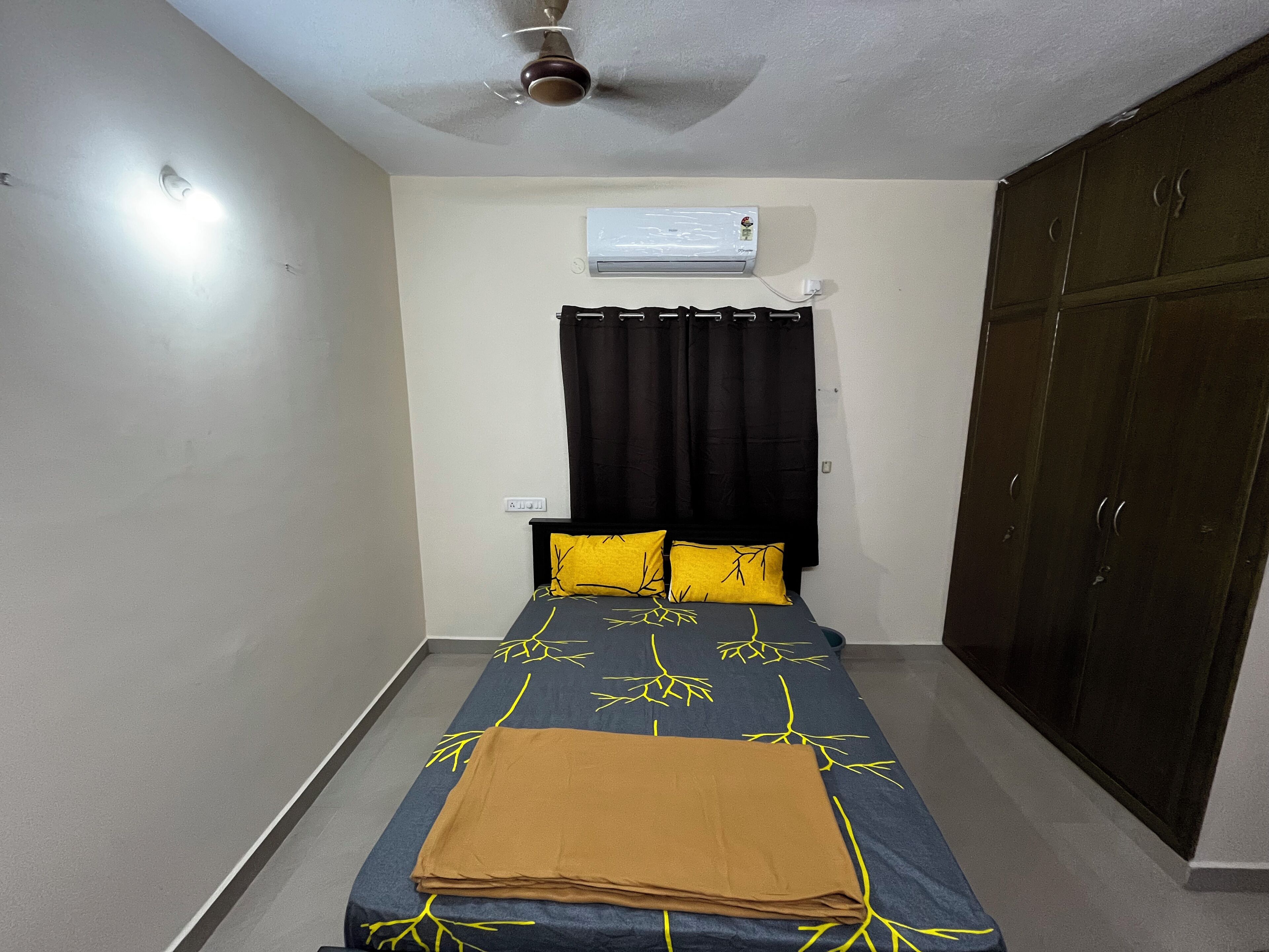 A bedroom with a bed, a ceiling fan, an air conditioning unit, and a wardrobe.