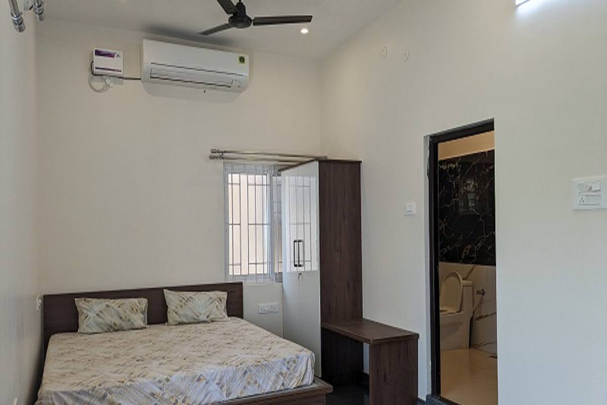 A bedroom with a bed, a desk, a wardrobe, and a bathroom visible through an open door.