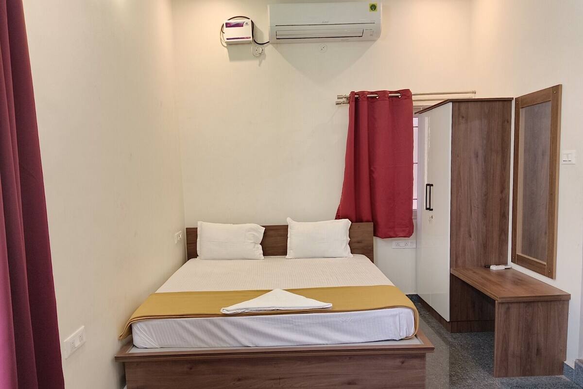 A single bed with a wooden frame, a bedside table, a red curtain, a wardrobe, and an air conditioning unit mounted on the wall.