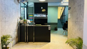 A hotel reception area with a reception desk, a clock, and a sign indicating check-in times. - Abodes Elegant Hills (Dehradun)