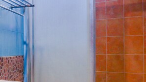A bathroom with a toilet, a shower area with orange tiles, and a blue tiled wall. - Hotel O Istana Griya 2 Hotel (Surakarta)