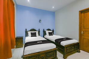 A bedroom with two wooden beds, a nightstand, a wall-mounted lamp, and a wooden door. - Hotel O Istana Griya 2 Hotel (Surakarta)