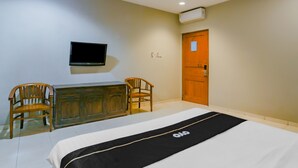A hotel room with a bed, two wooden chairs, a TV mounted on the wall, a wooden door, and an air conditioning unit. - Hotel O Istana Griya 2 Hotel (Surakarta)