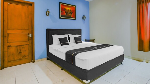 A bedroom with a bed, a wooden door, a wall-mounted artwork, and a nightstand. - Hotel O Istana Griya 2 Hotel (Surakarta)