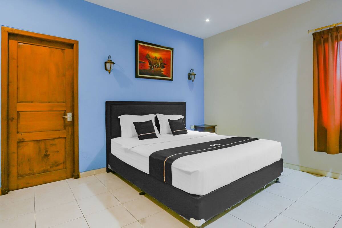 A bedroom with a bed, a wooden door, a wall-mounted artwork, and a nightstand.