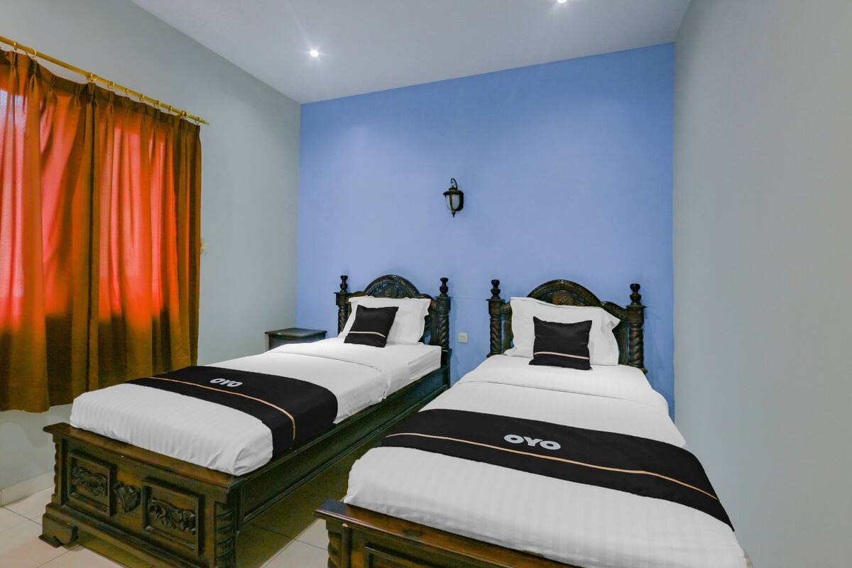 A hotel room with two wooden beds, each with a white and black bedspread, and a blue wall.