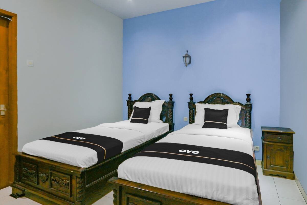 A double bed with a black and white bedspread and a logo, a nightstand, and a wall-mounted lamp.