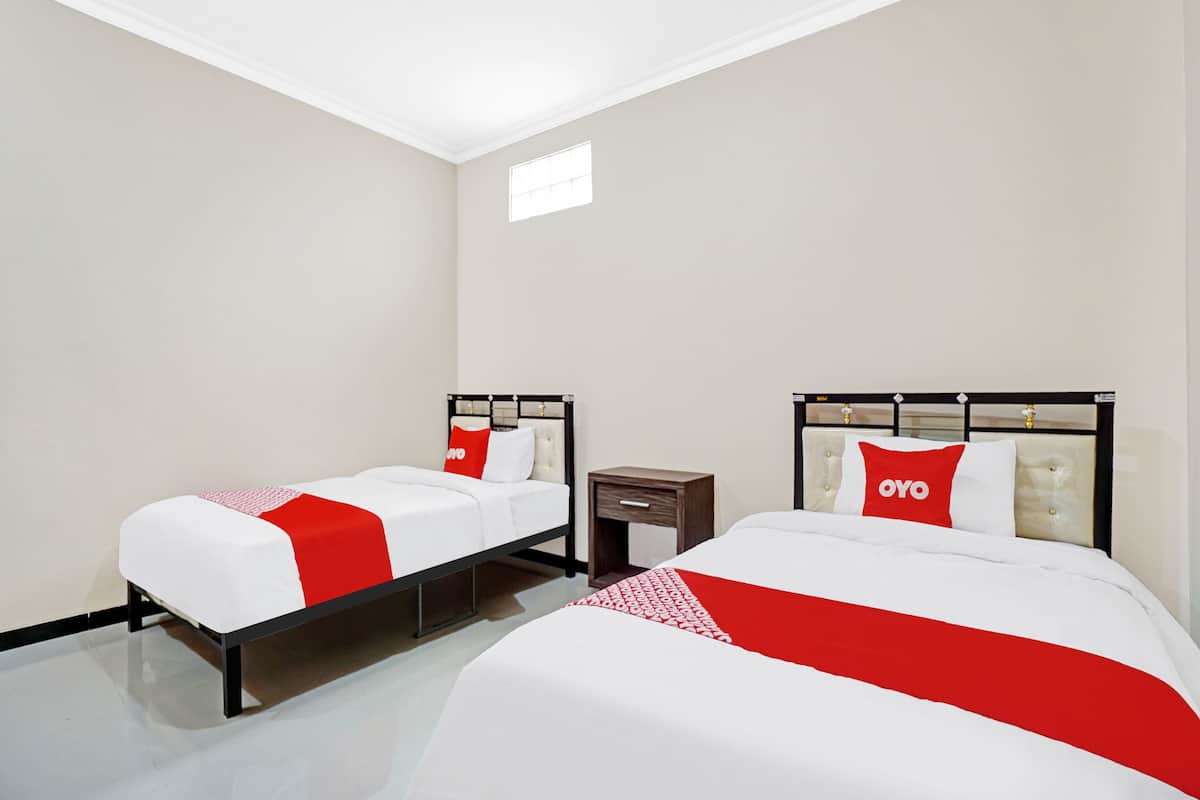 Ein Hotelzimmer mit zwei Betten, jeweils mit einer roten und weißen Bettdecke und passenden Kissen. Das Zimmer hat ein modernes Design mit weißer Decke und Wänden sowie einem kleinen Fenster, das natürliches Licht hereinlässt.