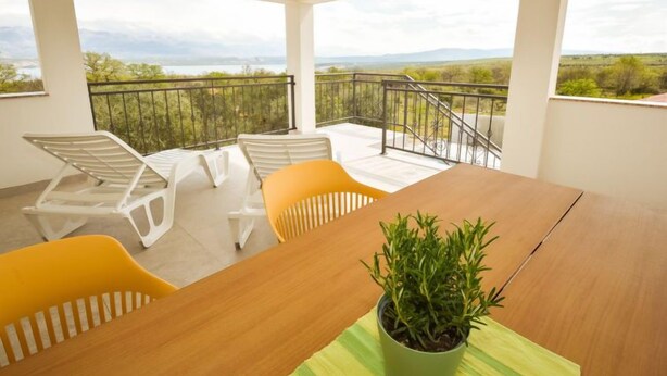 Un balcon avec vue sur la campagne, une table en bois et deux chaises.
