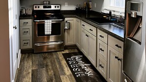 A kitchen with light-colored cabinets, stainless steel appliances, a wooden floor, and a welcome mat. - SC Farmstead Cottage with modern amenities, farm views, and equine visitors (Belton)