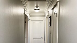 A hallway with a wooden floor, white walls, and a white door at the end. - SC Farmstead Cottage with modern amenities, farm views, and equine visitors (Belton)