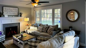 A living room with a fireplace, a ceiling fan, and a large window. - SC Farmstead Cottage with modern amenities, farm views, and equine visitors (Belton)