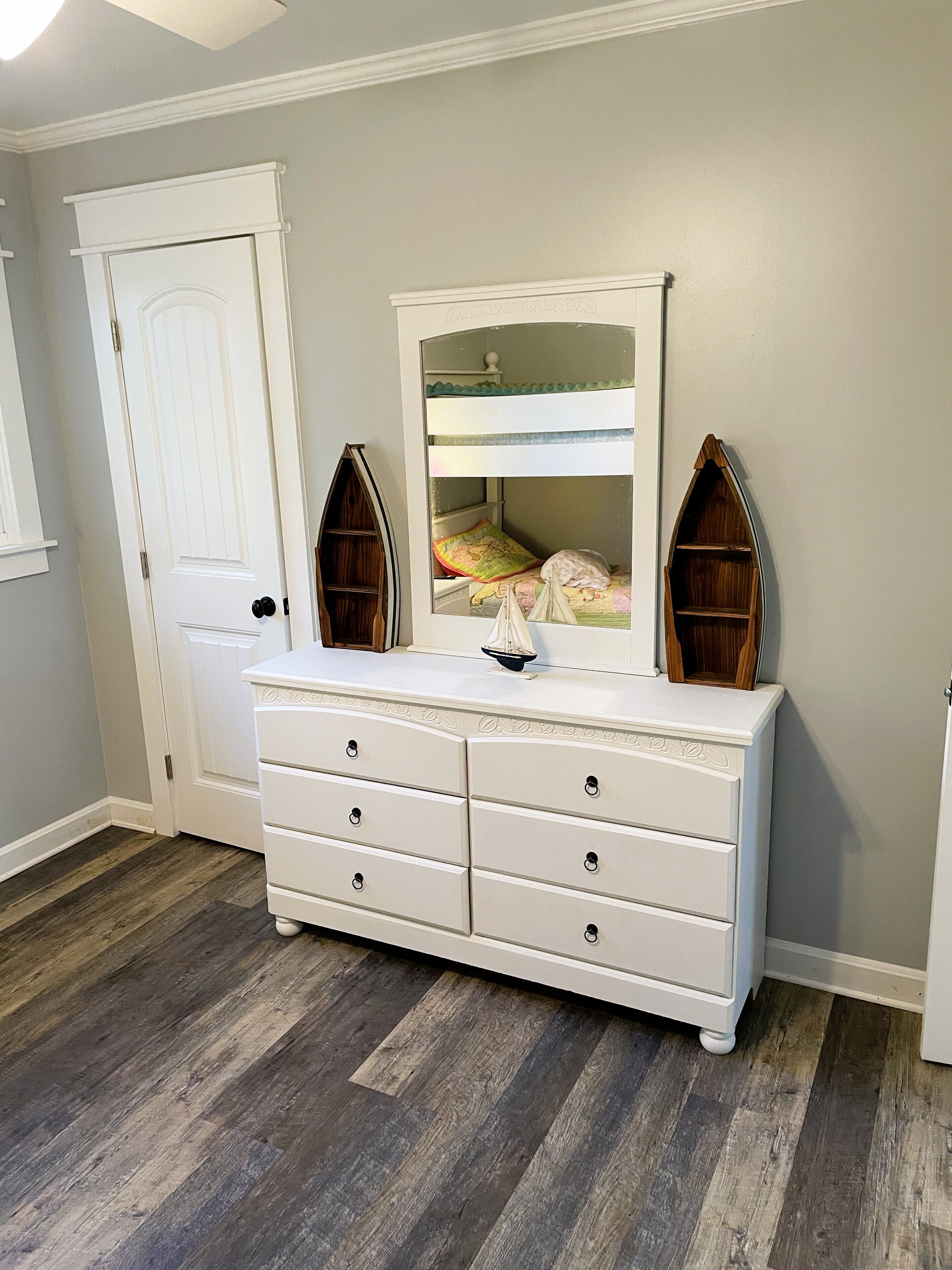 A bedroom with a white dresser, a bunk bed, and a wooden boat-shaped mirror.