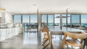 A modern dining area with a long table and chairs, large windows offering a view of the sea, and a clean, minimalist design.