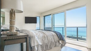 A modern bedroom with a large bed, a bedside table, a lamp, and a TV.