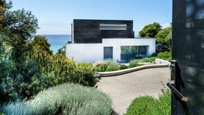 A modern house with a white facade, a dark upper section, and a gravel driveway leading to a garage.