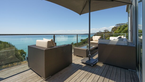 A deck with wicker furniture and a large umbrella, overlooking a body of water.
