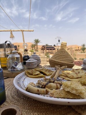 Una mesa dispuesta con platos tradicionales marroquíes, una cesta tejida y vistas al paisaje desértico.