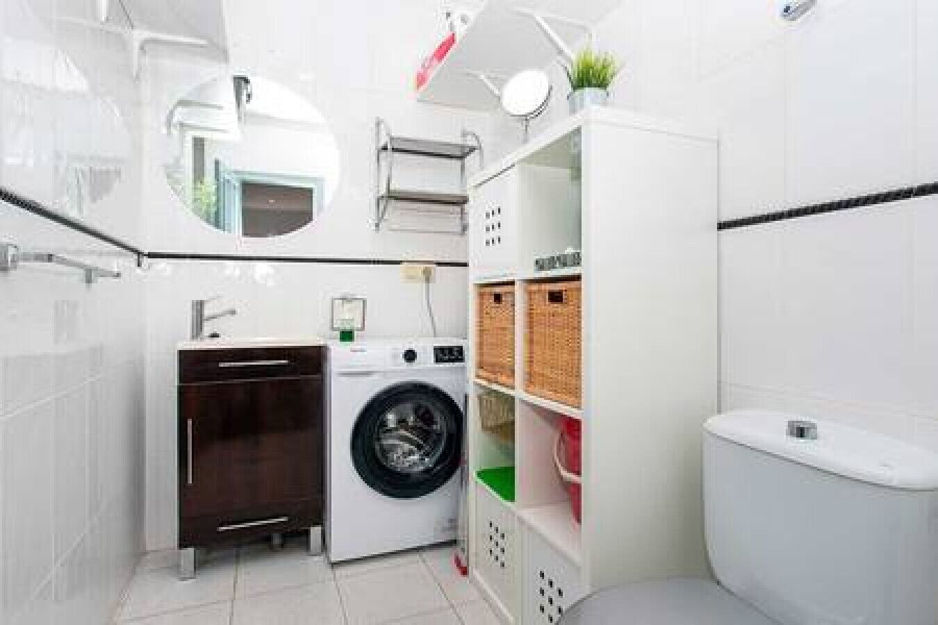A compact, modern bathroom with a washing machine, a toilet, and storage shelves.