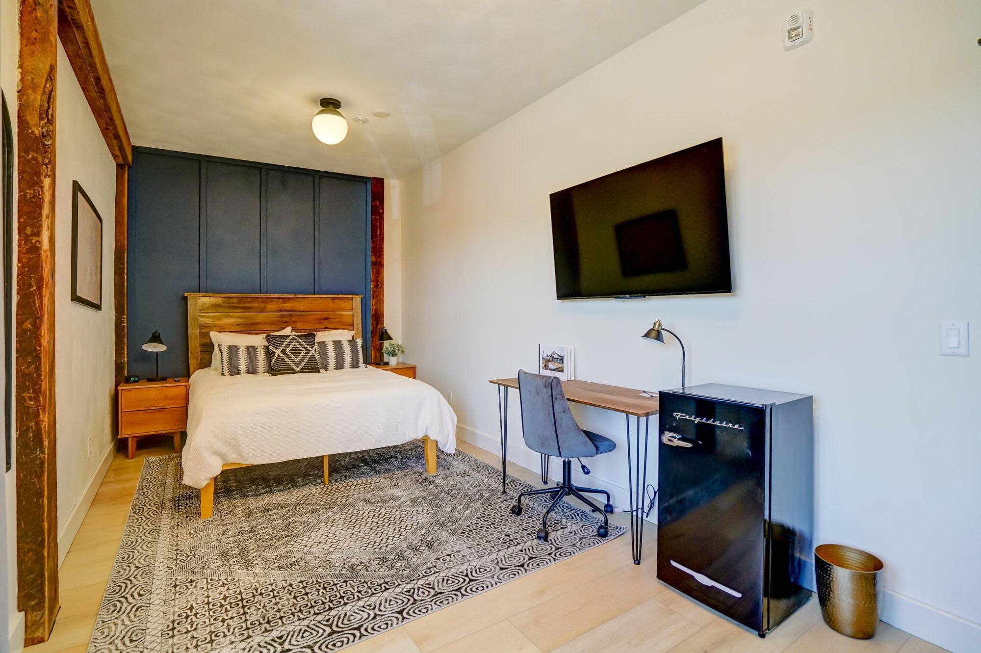 A bedroom with a bed, desk, chair, and a TV.