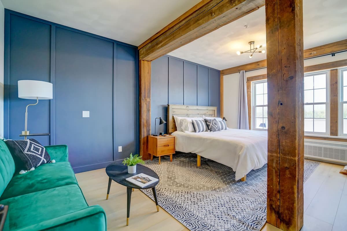 A bedroom with a bed, a nightstand, a lamp, a green sofa, and a window.