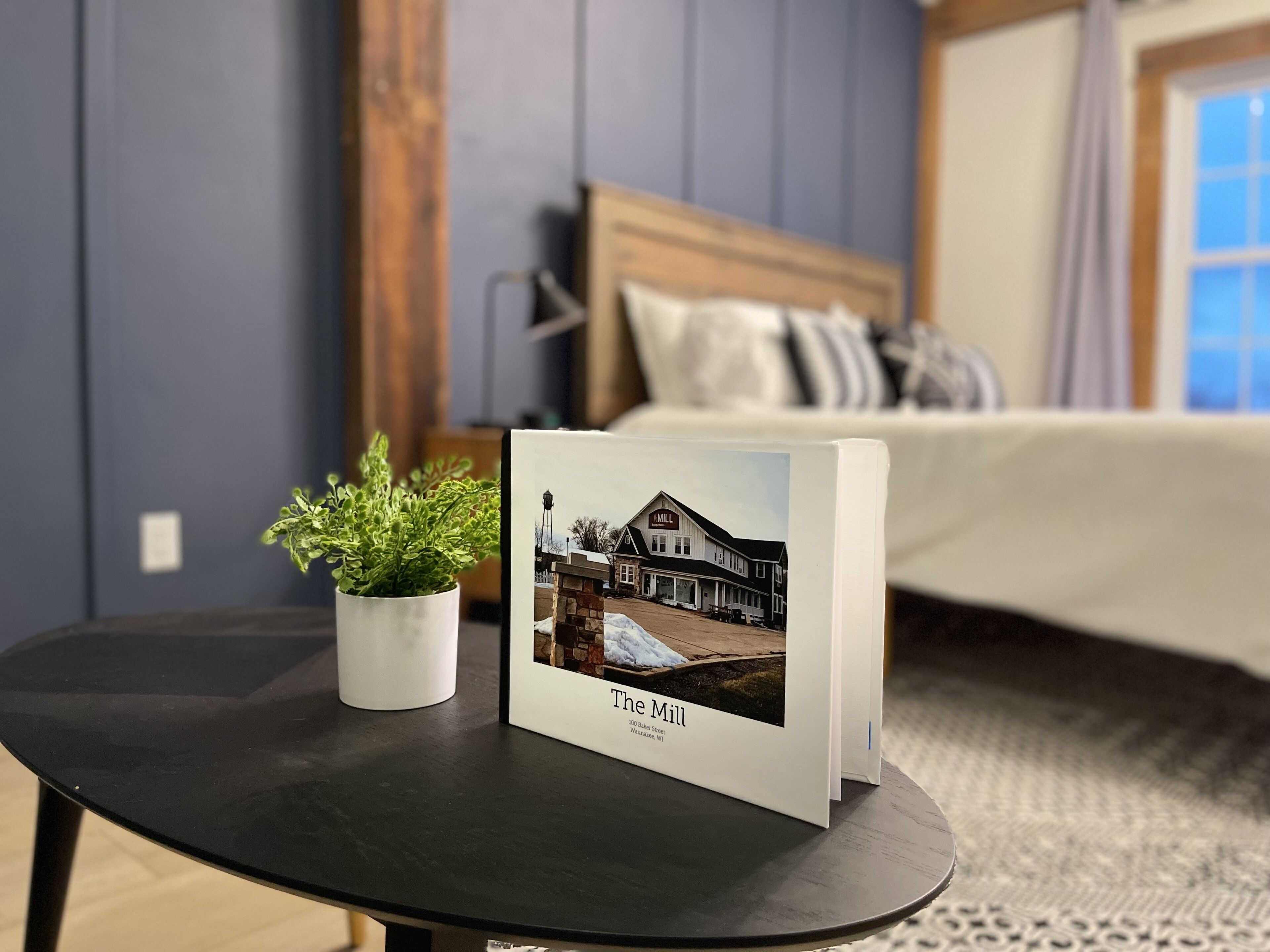 A framed photograph of a building labeled "The Mill" on a small table in a room with a bed and a window.